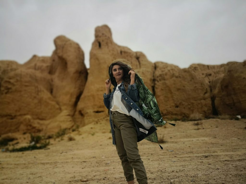 A woman standing before a dry desert landscape in cargo pants and a heavy jacket. 